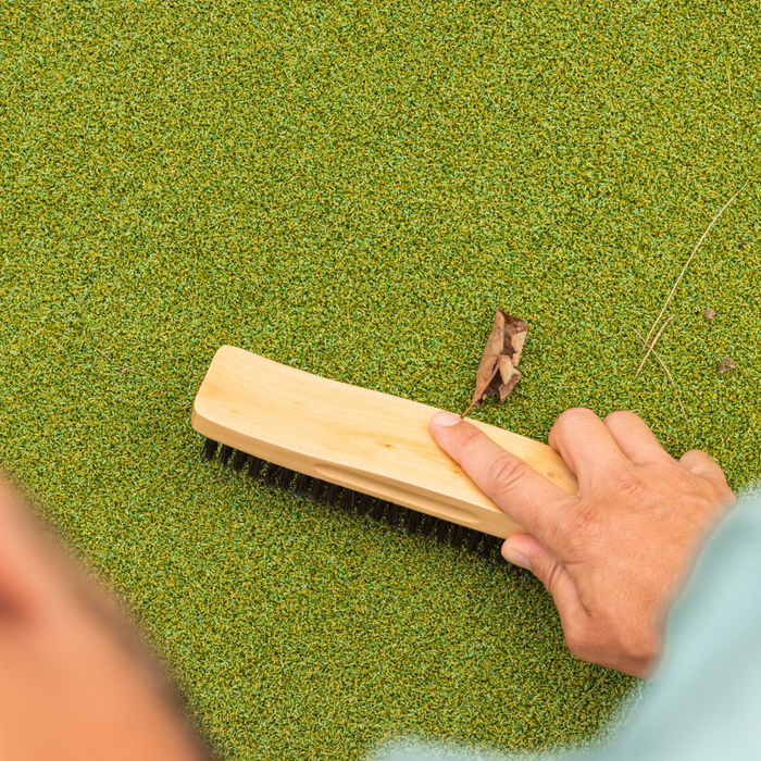 A person uses the BirdieBall Putting Green Stimp Maintenance/Slowing Brush to remove debris, like a dry leaf, from a RollTech putting surface.