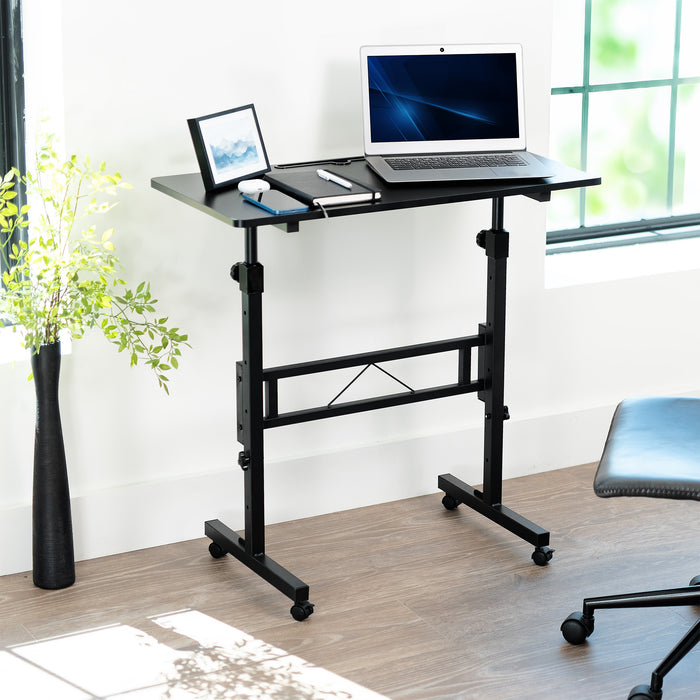 Adjustable standing desk with laptop on a wooden floor near a window.