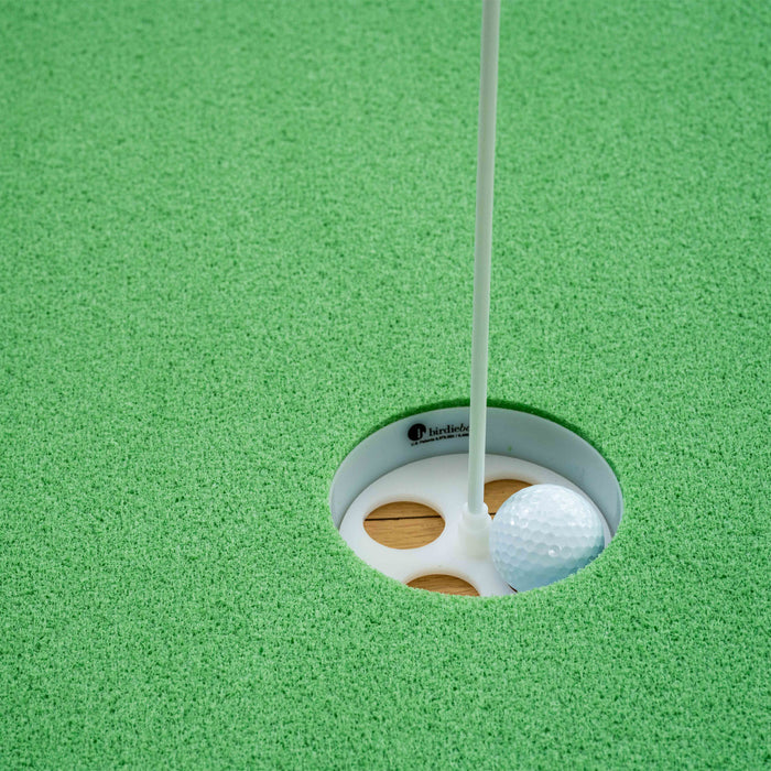 A BirdieBall Double Depth Putting Green Cup (1" Deep) holds a golf ball against the flagstick on green artificial turf.