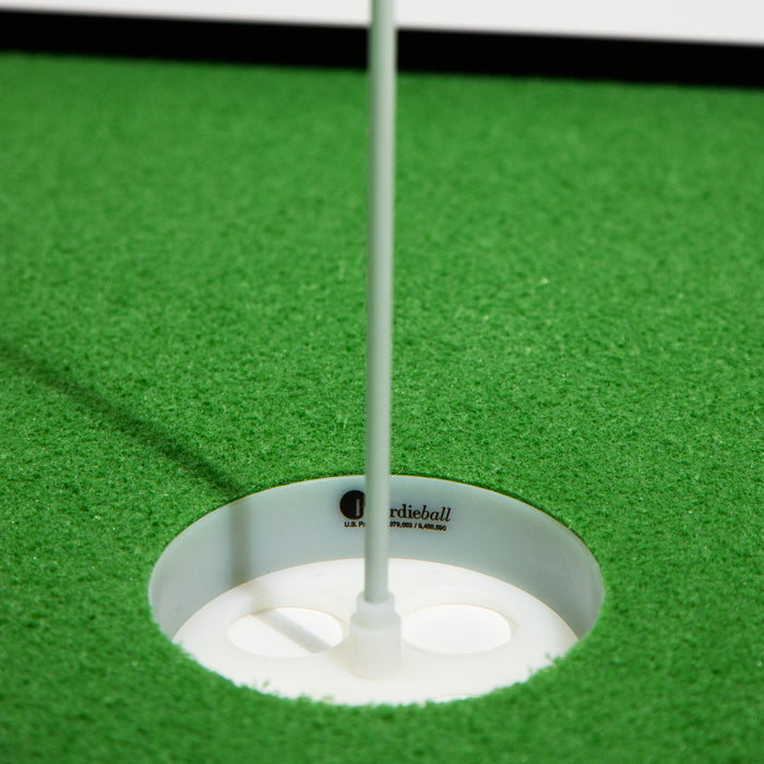 Close-up of a BirdieBall Double Depth Putting Green Cup (1" Deep) with a white flagstick on green artificial turf; "birdieball" branding appears inside the cup.