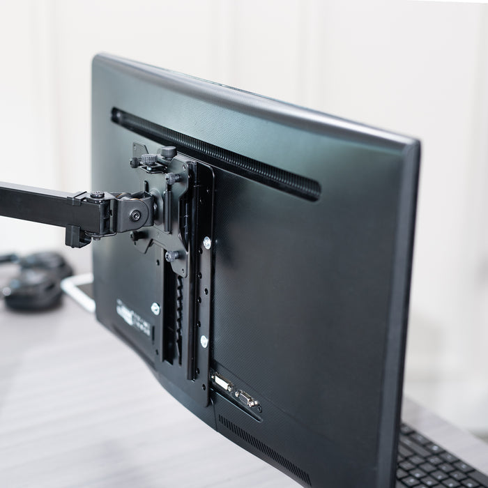 Height-adjustable Vesa adapter attached to a monitor on a desk with office background