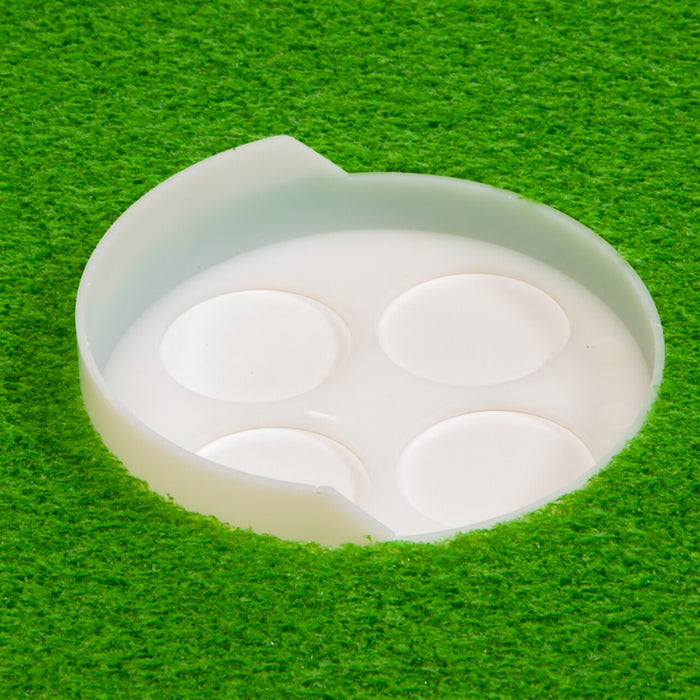 A close-up of a BirdieBall High Back Putting Green Cup (1/2" deep), a white plastic container holding four round white discs, shown on a textured bright green surface.
