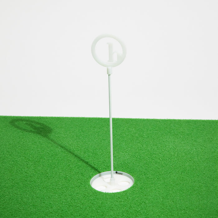 A BirdieBall Putting Green Cups and Flags set with a circular top stands on an artificial green surface, casting a leftward shadow—an ideal upgrade for your BirdieBall putting green accessories.