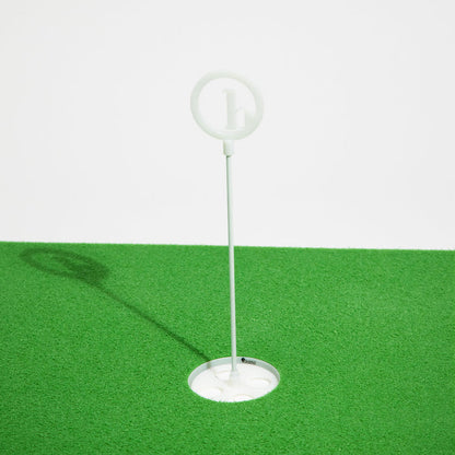 A BirdieBall Putting Green Cups and Flags set with a circular top stands on an artificial green surface, casting a leftward shadow—an ideal upgrade for your BirdieBall putting green accessories.