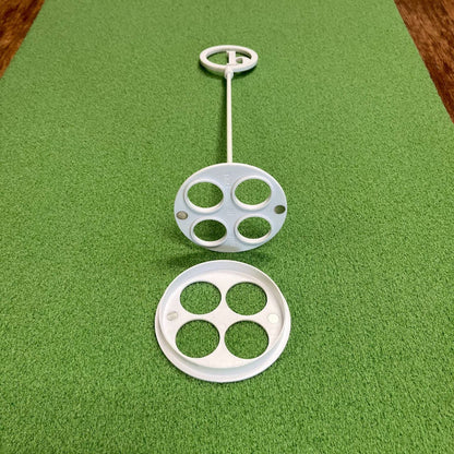 A BirdieBall Putting Green Cups and Flags set in white plastic, featuring circular holes, rests on a textured green surface with one cup separated and facing upward.