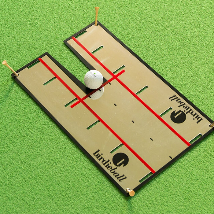 The BirdieBall Putting Mirror is a golf training aid featuring red alignment lines, an artificial green turf base, a golf ball, and tees for enhanced putting practice.