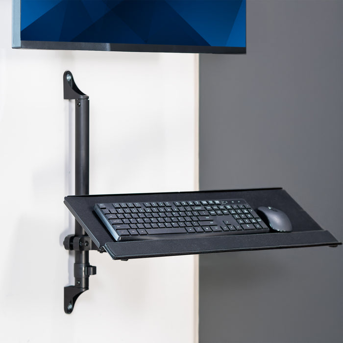 Wall-mounted keyboard tray with a keyboard and mouse on a gray wall.